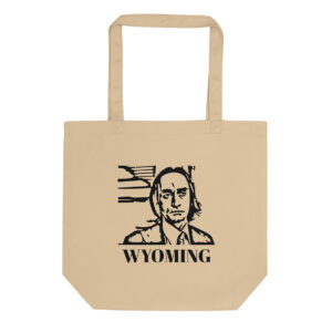 A beige canvas tote bag displays a black stencil-style portrait of a man in front of abstract lines, with the word “WYOMING” in bold capital letters beneath.
