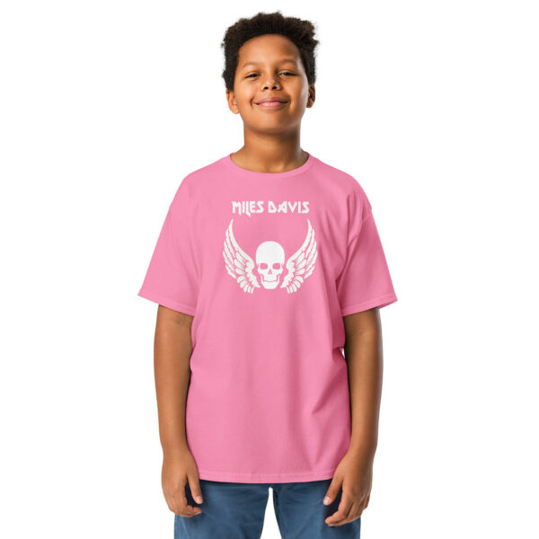 Front view of a light pink T-shirt with the same white “Miles Davis” winged skull design. The child stands in the same relaxed pose, smiling.