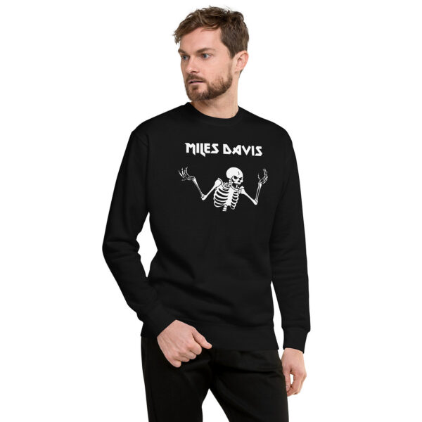 A man in a black sweatshirt featuring a white skeleton illustration and “Miles Davis” in angular type. He looks to the left with one hand in his pocket.