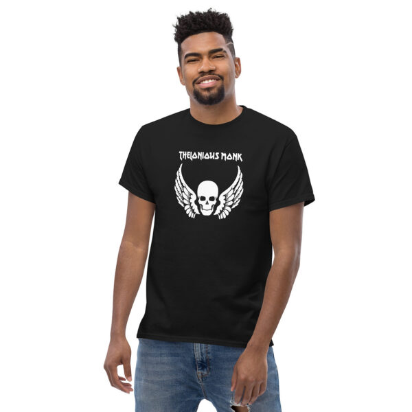 A man smiling and wearing a black t-shirt that showcases a white skull and wings graphic with “Thelonious Monk” printed in white text above.
