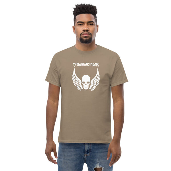 Man in taupe t-shirt with white graphic of winged skull and "THELONIOUS MONK" in blocky uppercase letters, standing against a white background.