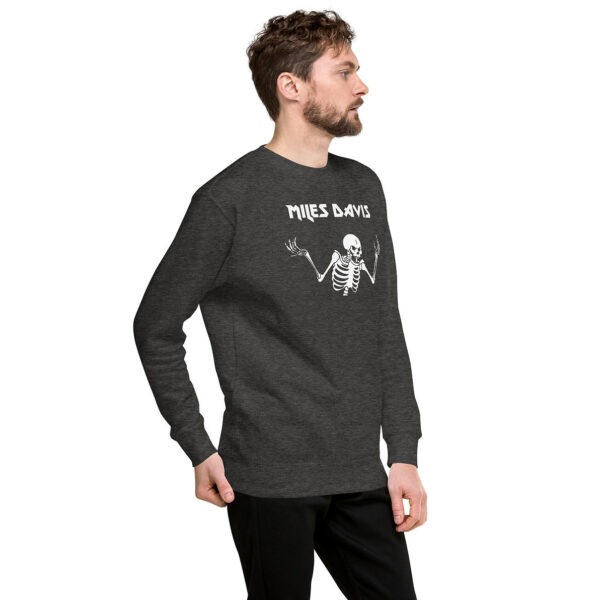 A man in a dark heather gray crewneck sweatshirt with a white skeletal figure and “Miles Davis” in sharp block letters. He stands sideways with hands behind his back.