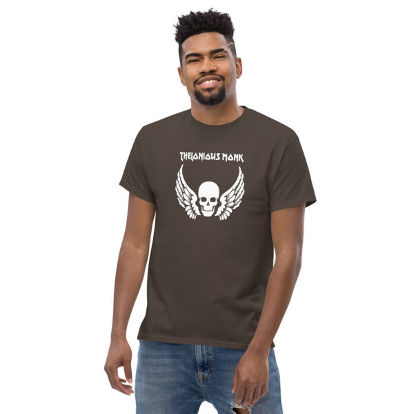 Man smiling in a brown t-shirt printed with a white winged skull graphic and “Thelonious Monk” in white stylized text above.