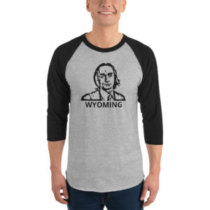 A man wears a heather gray and black raglan shirt with a black stencil-style face illustration and bold text reading “WYOMING.”