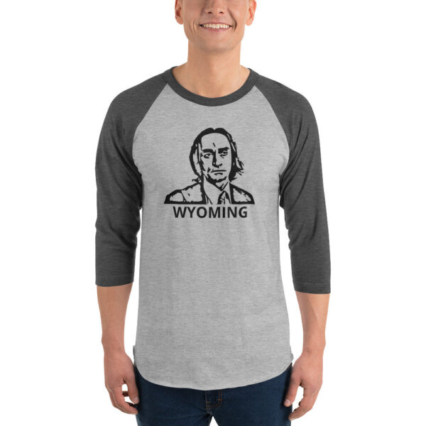 A man models a heather gray shirt with charcoal gray 3/4 sleeves, featuring a black stencil-style portrait and the word “WYOMING.”