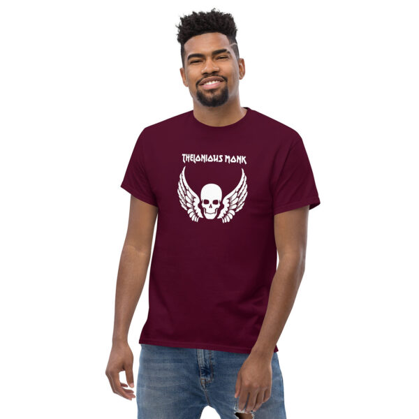 A man smiling in a maroon t-shirt featuring a white graphic of a skull with feathered wings and the words “Thelonious Monk” above it in white lettering.