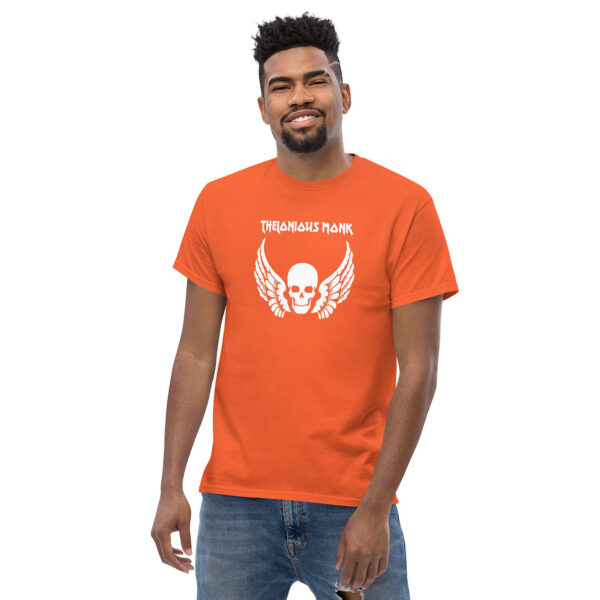 Man smiling in orange t-shirt with white winged skull graphic, featuring the text "THELONIOUS MONK" in jagged uppercase font above the image.