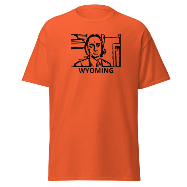 Orange t-shirt showing a black block-print-style illustration of a serious man in a suit and tie within a rectangular border, with the word “WYOMING” centered below.