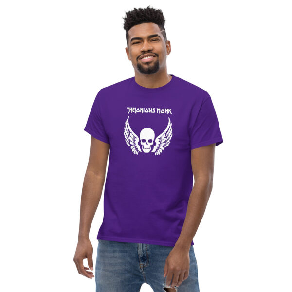 A man smiling while wearing a purple t-shirt that displays a white skull with angel wings and “Thelonious Monk” in bold, graphic white text above.