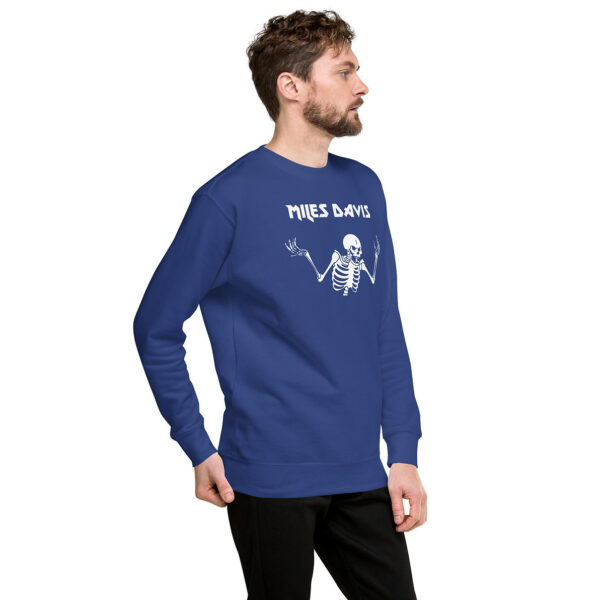 A man in a royal blue crewneck sweatshirt with a white skeleton design and “Miles Davis” in stylized font. He faces left with a relaxed posture.