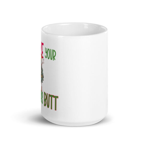 White ceramic mug partially displaying festive text in red and green, along with part of a cartoon image and the word “BUTT” in bold holiday-style font.