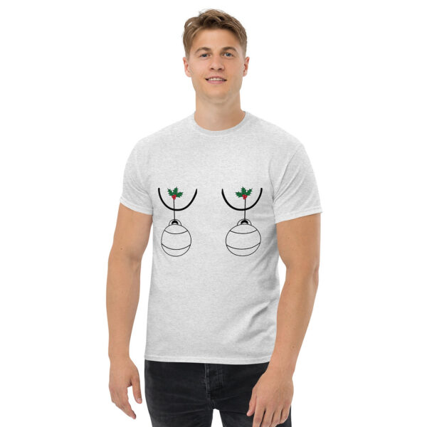 Man wearing a light gray T-shirt with a playful holiday design featuring two Christmas ornaments hanging from holly sprigs, positioned humorously over the chest.