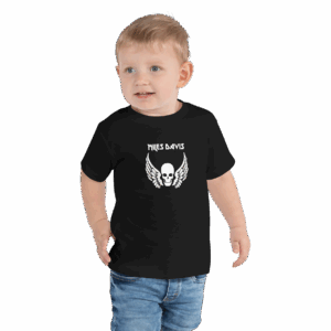 Toddler wearing a black T-shirt with a bold white graphic on the chest that features a skull with outstretched wings beneath the name "MILES DAVIS" in a stylized font. The child has short blond hair, is smiling, and is also wearing denim jeans.
