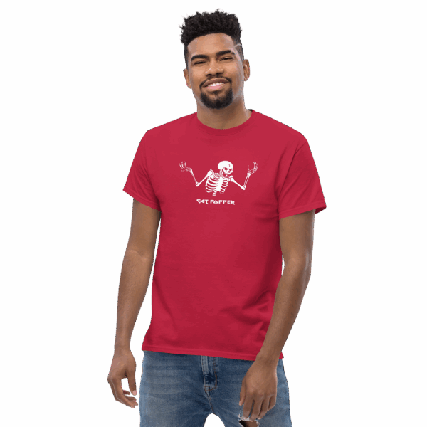 Man wearing a red t-shirt with a white skeleton graphic and the text "CAT POPPER" printed on the front, standing casually and smiling slightly.