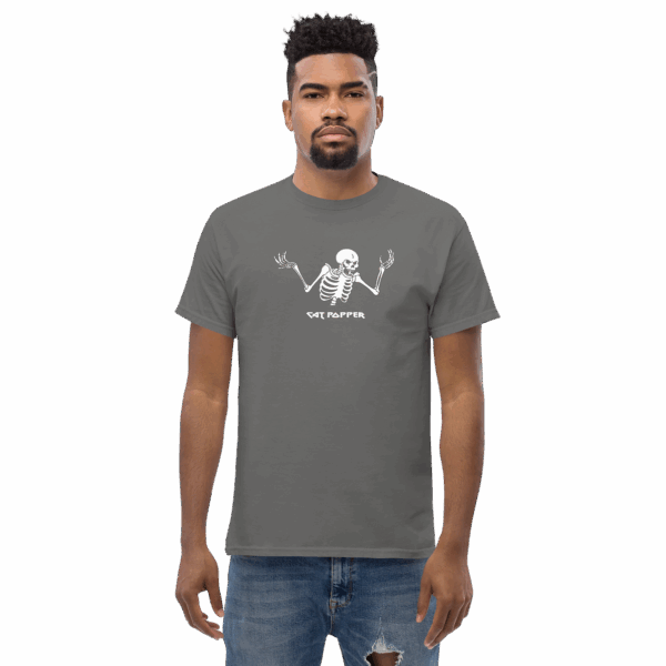 Man wearing a dark gray graphic t-shirt featuring a white skeleton with raised hands and the text "CAT POPPER"; he is standing and facing forward with a neutral expression.