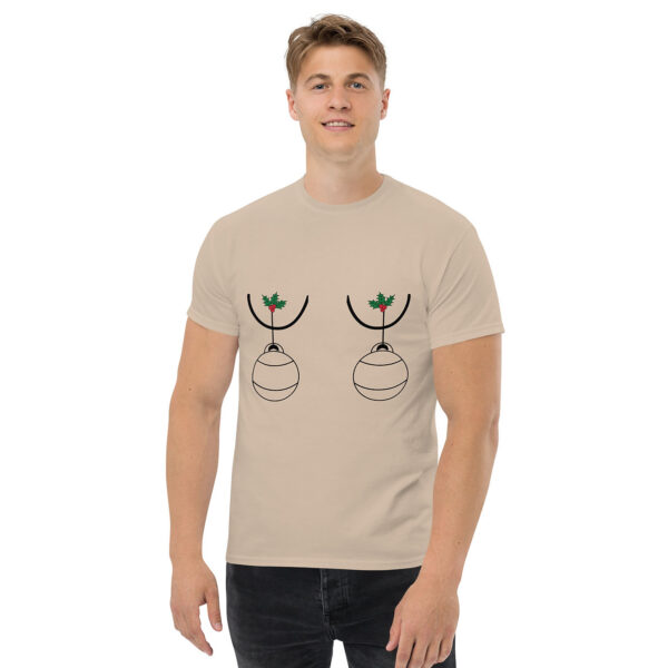 Man wearing a beige T-shirt featuring a playful holiday design with two Christmas ornaments hanging from holly sprigs, positioned over the chest.
