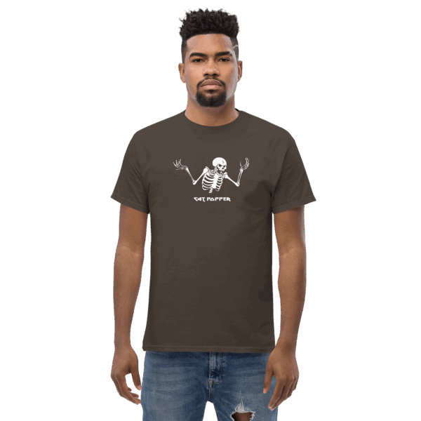 Man wearing a dark brown graphic t-shirt with a white cartoon skeleton illustration and the text “Cat Popper”; he is standing straight with a neutral expression facing forward.