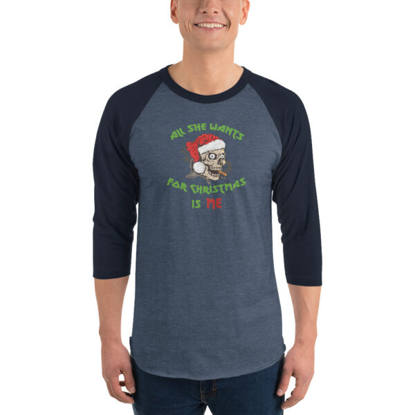 A man wearing a navy blue and heather denim 3/4 sleeve raglan shirt. The shirt features a graphic of a smoking skull in a Santa hat with green and red text that reads: "All She Wants For Christmas Is Me."