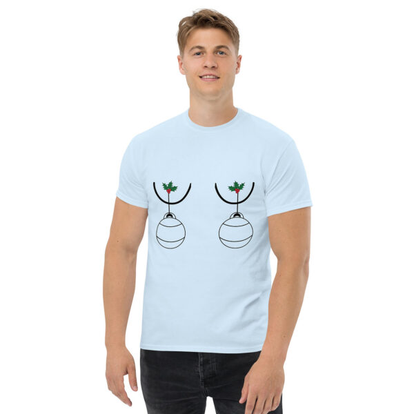 Man wearing a light blue T-shirt with a humorous Christmas design showing two ornaments hanging from holly sprigs, positioned over the chest.