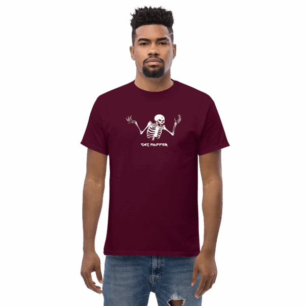 Man in a maroon graphic T-shirt displaying a white skeleton with raised hands and the words "Cat Popper" beneath the design, standing straight with a neutral expression against a plain background.