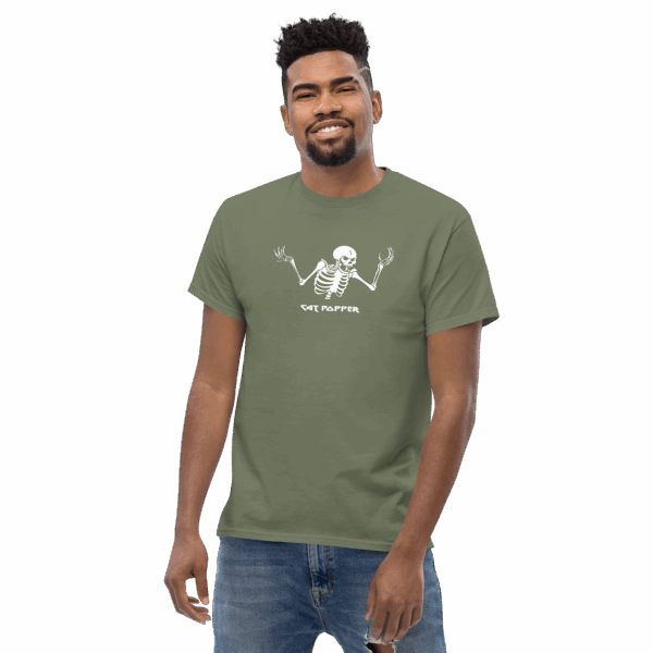 Smiling man wearing a moss green T-shirt with a white skeleton graphic and the text "Cat Popper" printed below, standing with one hand in pocket.