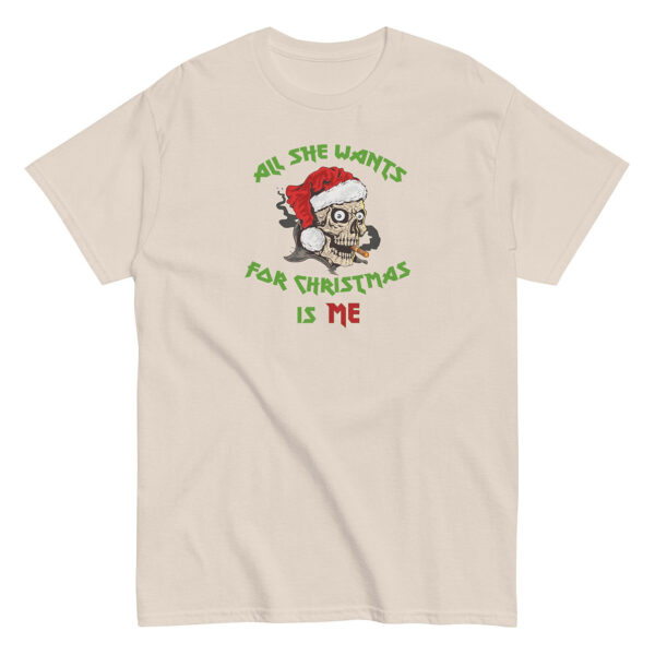 Beige short-sleeve t-shirt featuring a graphic of a cartoon skull wearing a Santa hat, smoking a cigar, with the phrase "All She Wants For Christmas Is Me" in bold green and red lettering curved around the image.