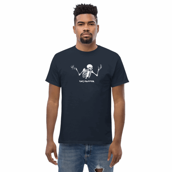 A serious-looking man wearing a navy blue T-shirt with a white skeleton illustration raising its arms and the words “Cat Popper” printed below, standing upright with hands at his sides.