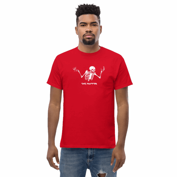 A man in a red T-shirt with a centered white graphic of a shrugging skeleton. The skeleton has its arms raised and palms turned upward in a questioning pose. Below the skeleton, the text reads “CAT POPPER” in a bold, white font. The man is standing straight with a neutral expression and is wearing distressed light blue jeans.