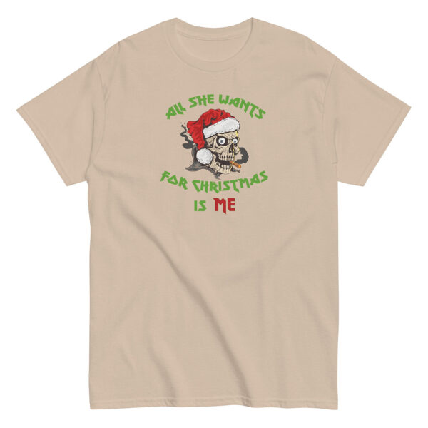 Sand-colored unisex T-shirt featuring a bold graphic of a smoking skull wearing a red Santa hat. Above and below the skull, green and red stylized text reads “All She Wants for Christmas Is Me.”