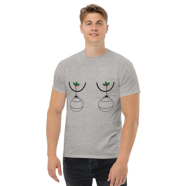 Man wearing a light gray T-shirt with a playful holiday design featuring two Christmas ornaments hanging from holly sprigs, positioned humorously on the chest.